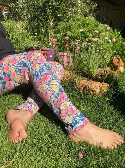 A girl sits on the grass wearing a pair of leggings with Carmel's watercolour design, "first bloom on navy."