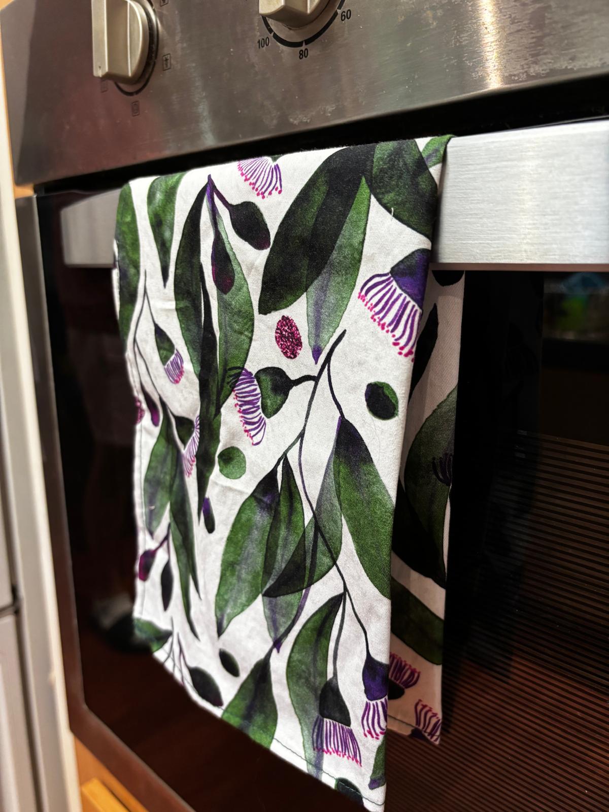 cotton tea towel with watercolour gum blossoms design hanging on an oven door